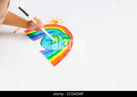 Il bambino disegna un pianeta del mondo con l'arcobaleno e il sole sul white paper. Disegni, dipinti e concetti per bambini. Istruzione e arte Foto Stock