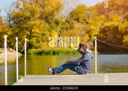 Il giovane si siede sul molo. Autunno giorno di sole. Vista laterale Foto Stock