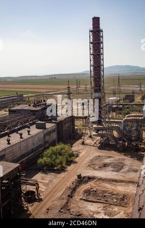 Vecchi edifici di fabbrica di metallurgia sovietica e camini arrugginiti su cielo blu e sfondo di montagna. Taraz città. Foto Stock