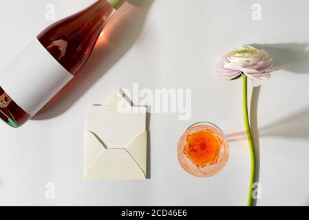 Cartolina di congratulazioni con bottiglia di vino rosato, fiore naturale tenero e cartolina di lettera in una busta su uno sfondo grigio chiaro con ombre, copia s. Foto Stock
