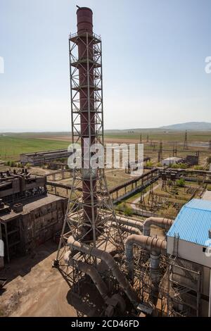 Vecchi edifici di fabbrica di metallurgia arrugginita e camino di fabbrica su cielo blu e montagne sfondo. Taraz città. Foto Stock