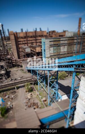 Vecchi edifici della fabbrica di metallurgia con trasportatore blu e camini di fabbrica su cielo blu. Vista dall'alto e obiettivo tilt-shift. Foto Stock