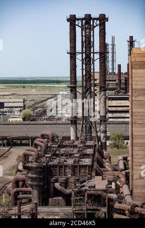 Obsoleta costruzione di una fabbrica di metallurgia sovietica e tubature arrugginite e camini sul cielo azzurro estivo. Taraz città. Foto Stock