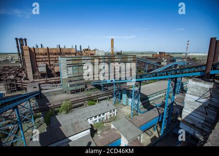 Edifici abbandonati della fabbrica di metallurgia con trasportatore blu e camini arrugginiti sul cielo blu. Vista aerea e panoramica. Taraz città. Foto Stock