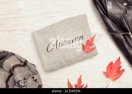 Maglia grigia con iscrizione Autunno, giacca nera, sciarpa e foglie autunnali. Concetto alla moda Foto Stock