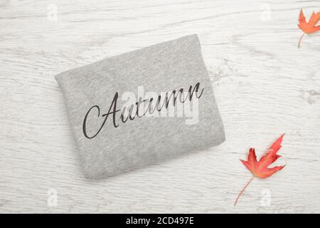 Pullover grigio con iscrizione Autunno su sfondo ligneo. Foglie d'autunno Foto Stock