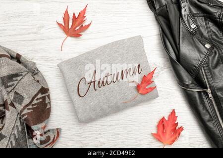 Maglia grigia con iscrizione Autunno, giacca nera, sciarpa e foglie autunnali. Concetto alla moda Foto Stock