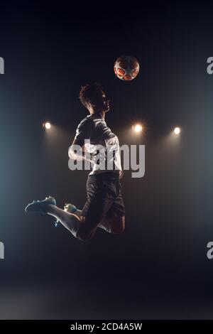 Calcio. Mulatto ragazzo in piedi isolato su sfondo nero archiviato saltando nebby sorridente felice Foto Stock