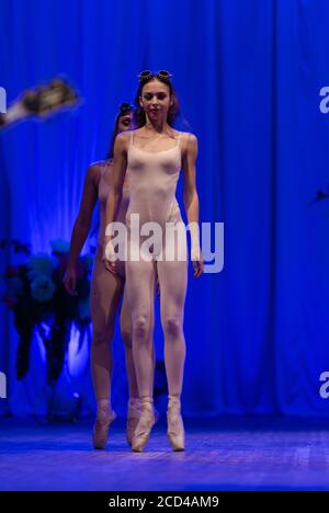 Ballerine e ginnastie di giovani donne con capelli lunghi dentro i costumi beige si esibiscono con uno spettacolo sul palco in un teatro su sfondo blu Foto Stock