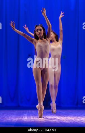 Ballerine e ginnastie di giovani donne con capelli lunghi dentro i costumi beige si esibiscono con uno spettacolo sul palco in un teatro su sfondo blu Foto Stock