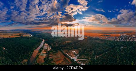 Vista panoramica dei colorati balloni ad aria calda che volano sul parco e sul fiume nella piccola città europea al tramonto estivo, nella regione di Kiev, Ucraina Foto Stock