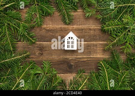 Piccola casa bianca su sfondo di legno. Telaio di rami di abete Foto Stock