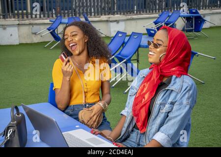 Donne africane sorridenti e shopping online mentre si siede in un caffè Foto Stock