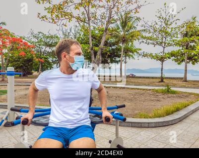 L'uomo che fa esercizi fisici, spingi, esercizi di forza, si appoggia in vuoto esterno parco pubblico della città palestra metallo indossare maschera da solo per Covid19 Foto Stock
