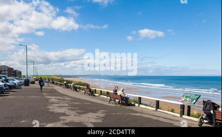 La gente sedette sulle panchine sul lungomare ammirando la vista A Saltburn dal mare, Inghilterra, Regno Unito Foto Stock