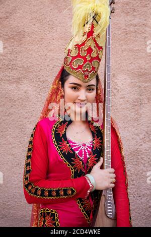 Uyghur ragazza in abito tradizionale rosso che tiene satar, cinese lungo collo piegato liuto nella città Kashgar / Kashi / Kasjgar, Xinjiang, Cina Foto Stock