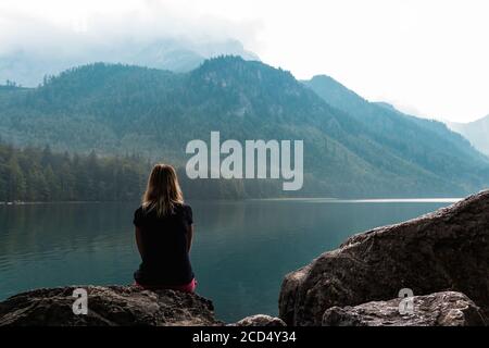 Bellezza giovane donna dalla schiena seduta sulla roccia a Vorderer Langbathsee lago in Austria Alp montagna Foto Stock