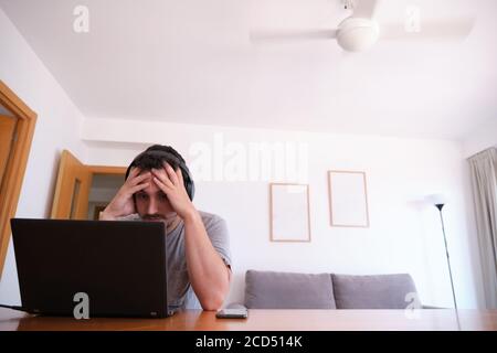 Giovane uomo che indossa le cuffie guardando serie, video, lezioni online su un computer portatile con il ventilatore acceso. Studiare online e e-learning concetto. Foto Stock