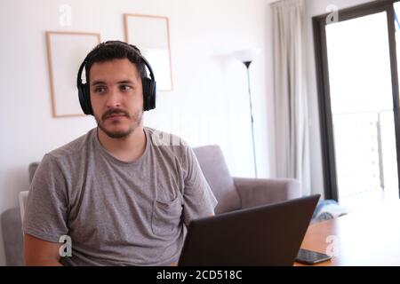 Il giovane uomo che indossava le cuffie distracted guardando serie, video, invece le sue classi in linea. Studiare online e e-learning concetto. Foto Stock