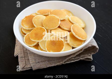 Mini Pancake fatti in casa cereali in un recipiente bianco su una superficie nera, vista laterale. Primo piano. Foto Stock