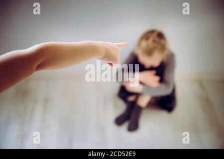 Bambino bullo che punta il dito contro il bambino della vittima sfocato irriconoscibile che si siede sul pavimento e piange. Concetto di bullismo. Foto Stock