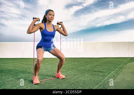 Donna di esercizio con allenamento elastico in palestra all'aperto. Ragazza asiatica che fa la resistenza che si allenano fuori su erba. Adatta lo stile di vita delle persone. Squat Foto Stock
