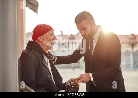 L'uomo anziano povero che indossa il cappotto, sofferente di tempo freddo incontra l'uomo ricco in strada, che lo ha aiutato con i soldi Foto Stock