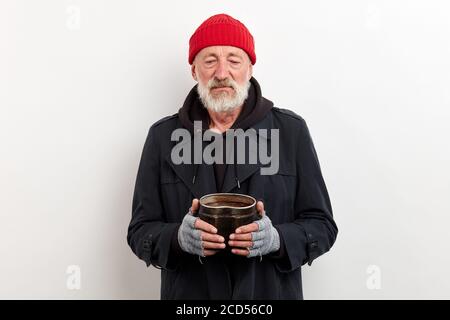 Il bum maturo in cappotto nero e il cappuccio rosso sulla testa che tiene la lattina di ferro per sollevare i soldi. Isolato su sfondo bianco Foto Stock
