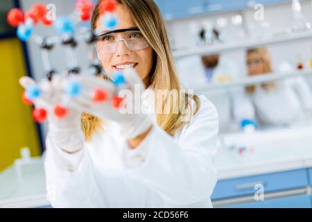 La chimica femminile con occhiali di protezione mantiene il modello molecolare in laboratorio Foto Stock