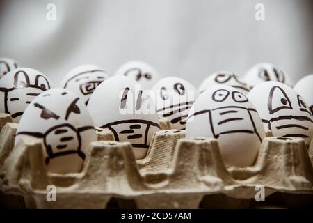 primo piano di diverse uova di pasqua di pollo con doodle facce indossare maschere mediche con sfondo bianco. Foto Stock