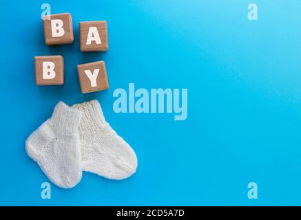 Baby testo su cubetti di legno e paio di graziose calze a maglia su sfondo blu. Concetto neonato. Disposizione piatta, vista dall'alto con spazio per la copia. Foto Stock