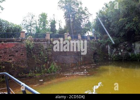 Ponte vecchio e surcresciuto sul canale di Bridgewater (fiume marrone) in una giornata di sole nel villaggio di Worsley, Inghilterra Foto Stock