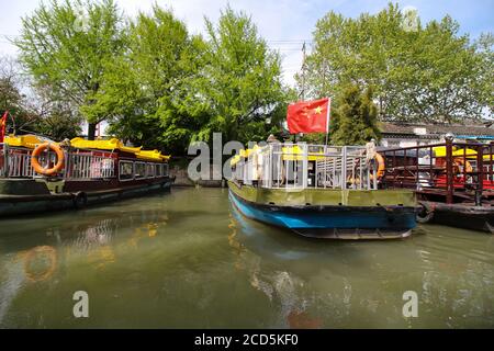 Canale in Cina Suzhou con barche ormeggiate lungo il banche con alberi e case sullo sfondo Foto Stock