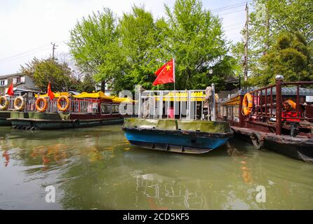 Canale in Cina Suzhou con barche ormeggiate lungo il banche con alberi e case sullo sfondo Foto Stock