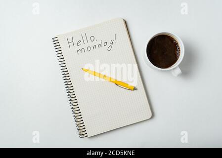 Ciao lunedi scritto su notebook su sfondo bianco. Caffè del mattino e programmi. Foto Stock