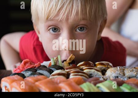 Divertente ragazzo dai capelli lonesti fissa Sushi. Bambino nel concetto di caffè. Cucina Asiatica. Foto Stock