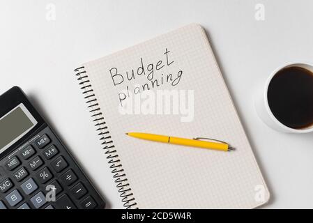 Pianificazione del budget di denaro. Testo scritto a mano. Notebook con calcolatrice e tazza di caffè su sfondo bianco Foto Stock