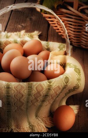 Ancora vita di un cesto pieno di uova marroni in una casa colonica rustica come impostazione, con luce laterale calda. Foto Stock