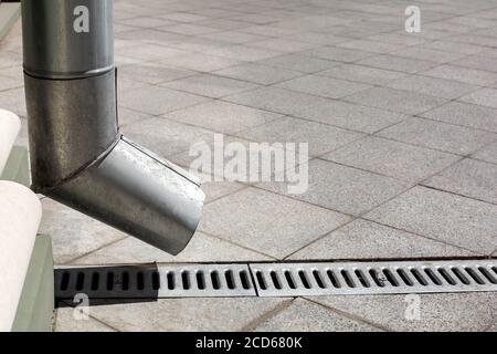 struttura di ingegneria di strada un tubo discendente con gocciolatoio di drenaggio su uno sfondo di un marciapiede grigio di granito di pietra da piastrelle quadrate con spazio di copia, Foto Stock