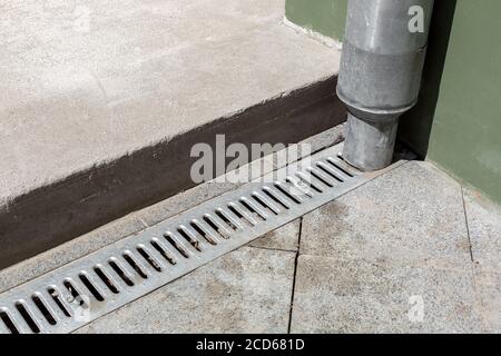 struttura ingegneristica tubo discendente su facciata edificio con grata di drenaggio di pavimento in pietra grigia e con soglia di cemento, dettagli closeup urbano in Foto Stock