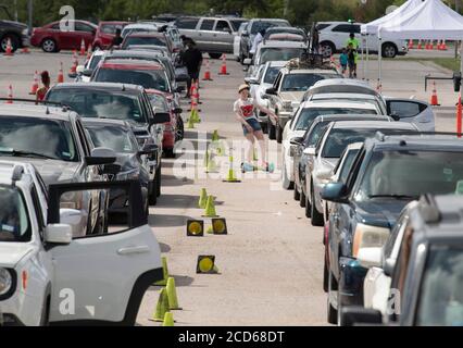 Austin, Texas USA 26 agosto 2020: Centinaia di auto dalla costa orientale del Texas e sud-ovest della Louisiana aspettano in fila un centro di evacuazione dell'uragano Laura presso l'area di parcheggio del circuito delle Americhe. Dopo aver trascorso ore a bordo del veicolo di famiglia, questo bambino ottiene un po' di aria fresca guidando uno scooter hoverboard autobilanciato. Laura dovrebbe fare la caduta di terra durante la notte come una tempesta di categoria 4 e devastare lungo le coste del Texas e della Louisiana e l'entroterra. Credit: Bob Daemmrich/Alamy Live News Foto Stock