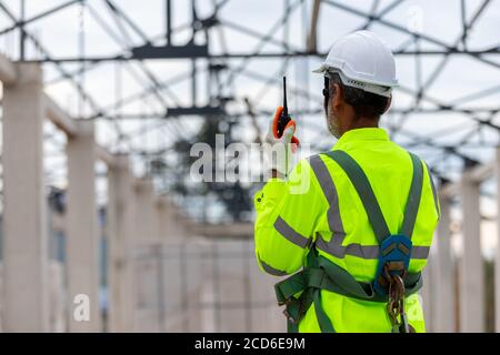 Ingegnere asiatico tecnico che guarda il controllo della costruzione nella costruzione di Strutture di tetti in cantiere un progetto di costruzione incompiuto Foto Stock