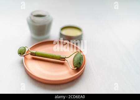 Prodotti di bellezza coreani per la cura della pelle di lusso - creme, giare con maschera di balsamo e fango con massaggiatore a rullo in pietra di giada - terapia massaggiante con rullo facciale Foto Stock