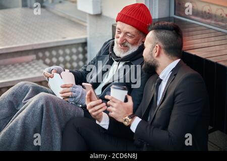 Felice ricco maschio e povero maschio guardare telefono ridendo, sorriso Foto Stock