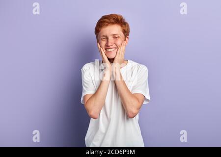 felice giovane allegro con un sorriso togoteo che tocca la guancia e soddisfatto di radersi la barba. primo piano ritratto, isolato sfondo blu Foto Stock