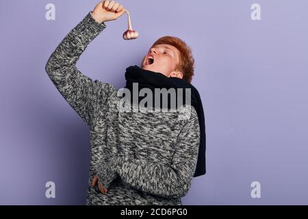 uomo malato che va mangiare aglio.uomo che lotta contro le malattie infettive e l'influenza. Primo piano. Concetto sanitario. Primo piano ritratto, sfondo blu isolato Foto Stock