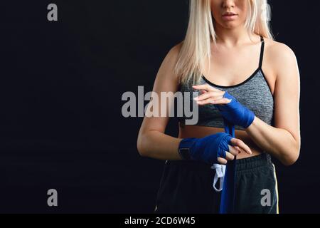 Bella bionda caucasica Muay Thai combattente avvolgendo le mani con una band, preparandosi in pugilato arena sport Foto Stock