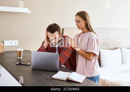 Triste uomo insoddisfatto con barba spessa vestita di camicia rossa, mette testa a portata di mano, legge messaggio sgradevole, fissa a schermo computer portatile, ritratto, io Foto Stock