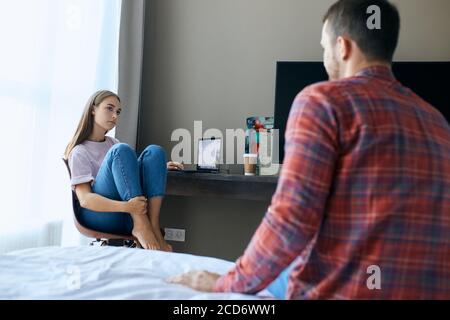 Giovani graziosi amanti che parlano in camera da letto, discutere i progetti futuri, attraente donna con capelli lunghi e casualmente vestito guarda via, parlando con impressv Foto Stock