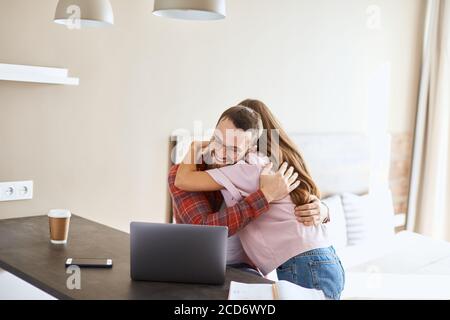 Uomo e giovane donna impressionanti con capelli lunghi si abbracciano teneramente, esprimono emozioni positive, felici di ricevere piacevoli notizie dai bambini, siediti dentro Foto Stock